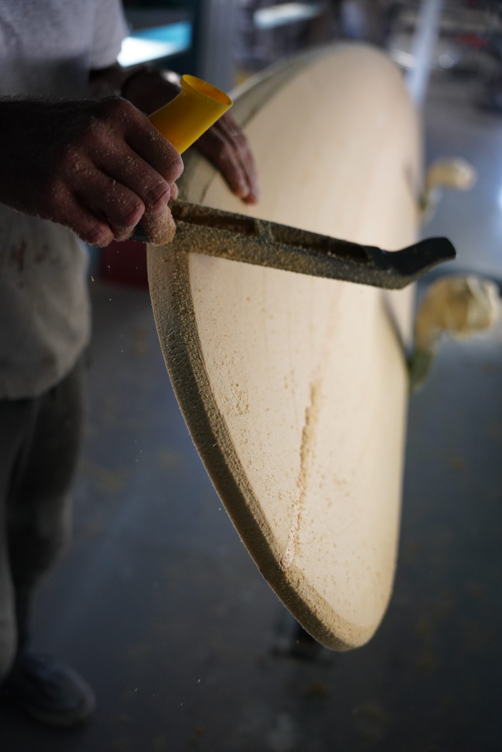 Shaper is using a surform to work on the nose of the surfboard